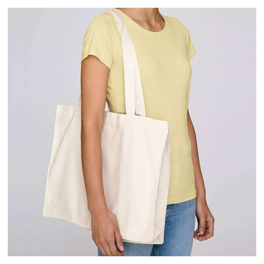 Person im gelben T‑Shirt trägt großen naturfarbenen Stoffbeutel über der Schulter