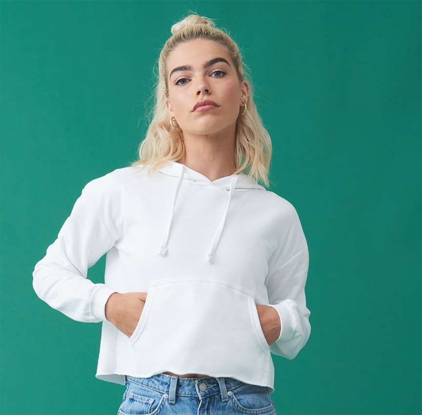 Junge Frau mit blondem Dutt in weißem Hoodie, Hände in Kängurutasche, grüner Hintergrund