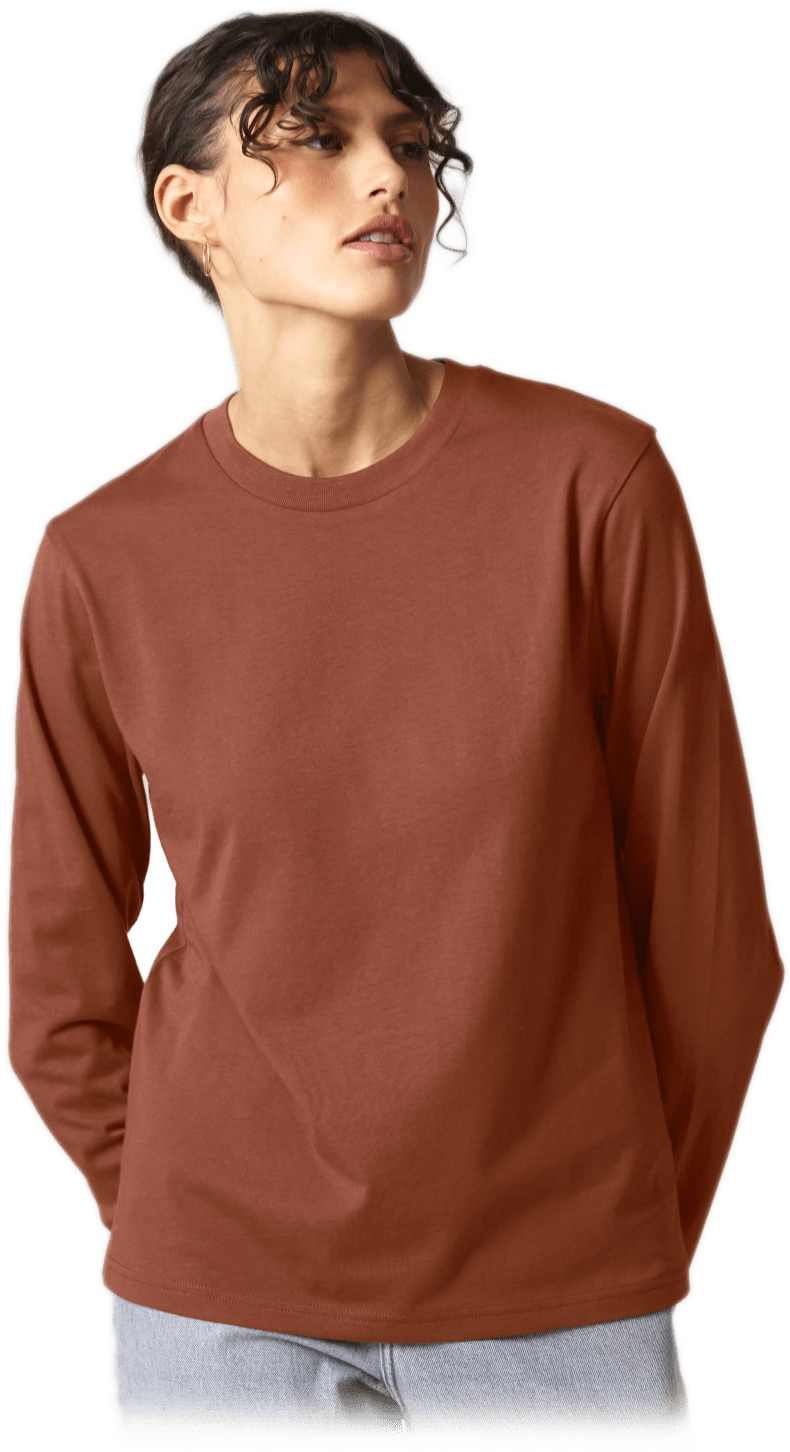 Person mit lockigem Haar trägt rostfarbenes Langarmshirt und helle Jeans, schaut zur Seite.